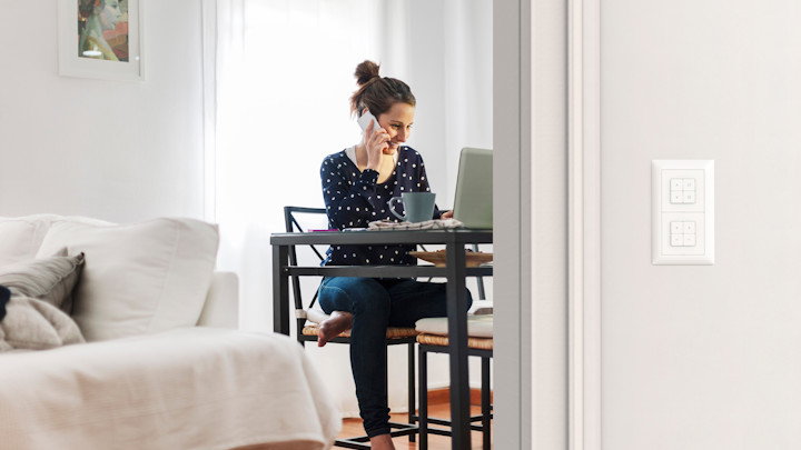 Ein telefonierende Frau sitzt an ihrem Schreibtisch in einer Wohnung