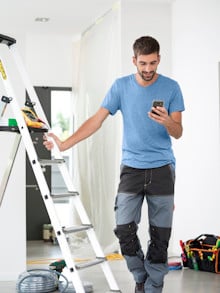 Elektriker mit Smartphone an einer Leiter lehnend.